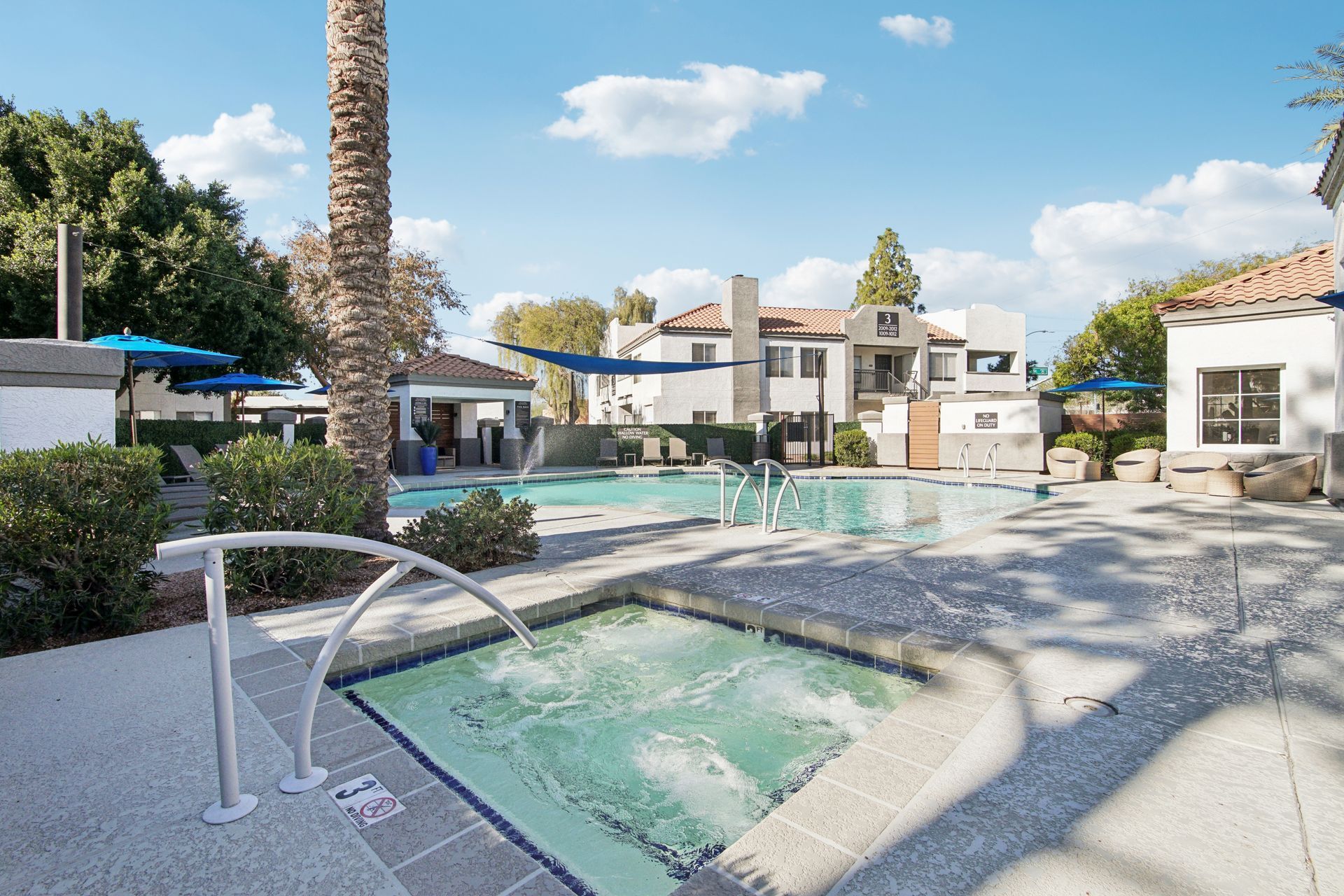 Pool area with a hot tub and buildings under a sunny sky.