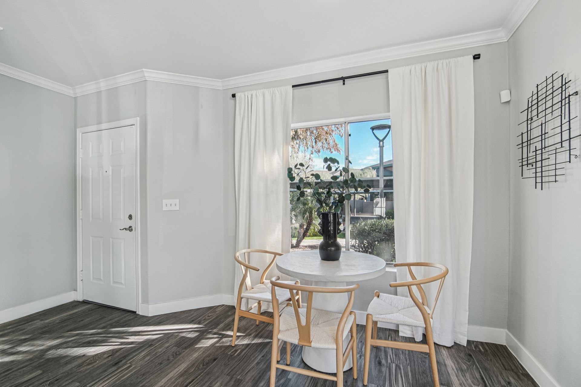 Dining area with white table, chairs, curtains, and a view through a window.
