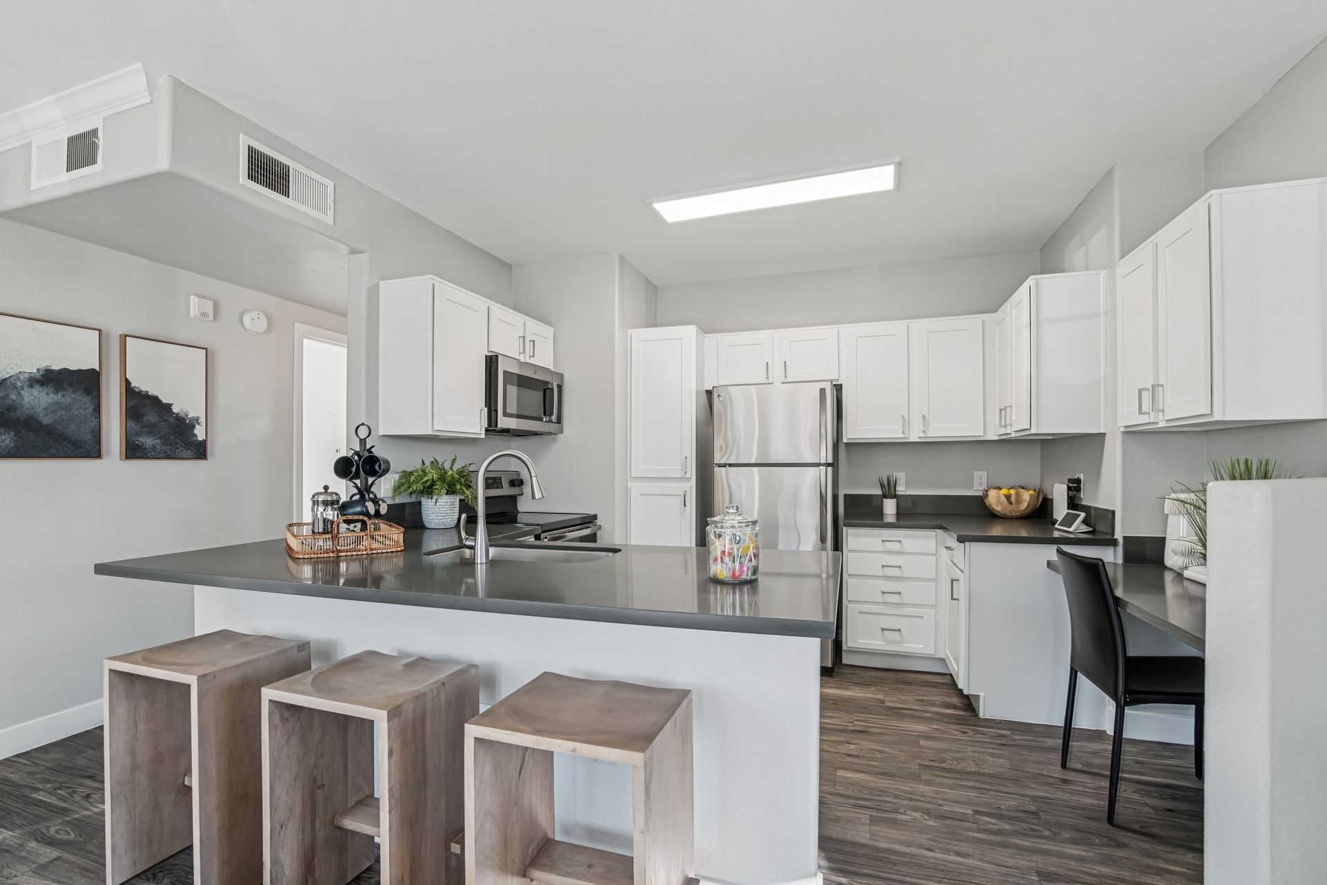 Modern kitchen with white cabinets, stainless steel appliances, dark countertop, breakfast bar with stools.