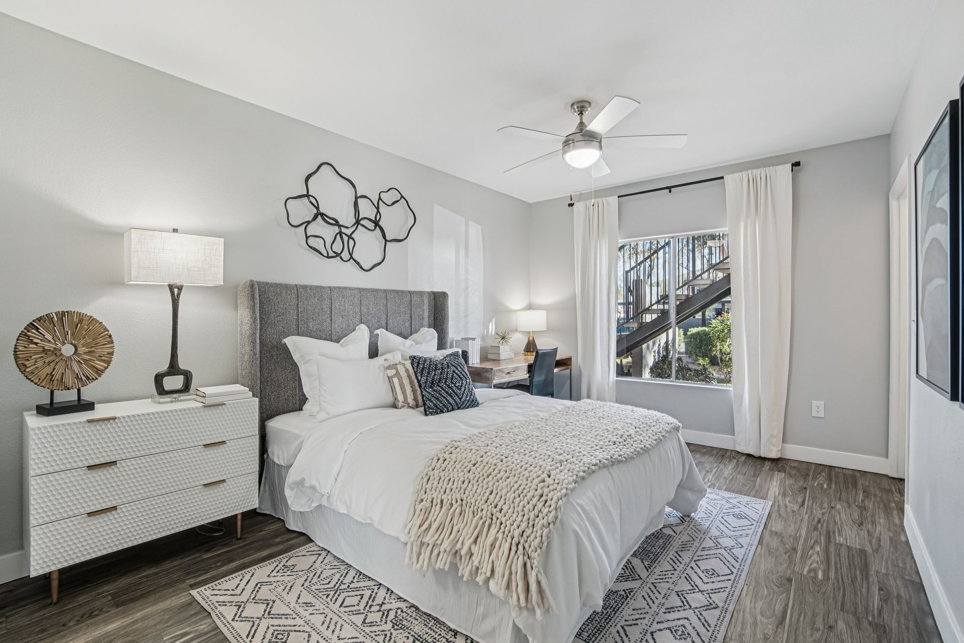 Bedroom with bed, nightstands, rug, window with stairs outside, art and ceiling fan.