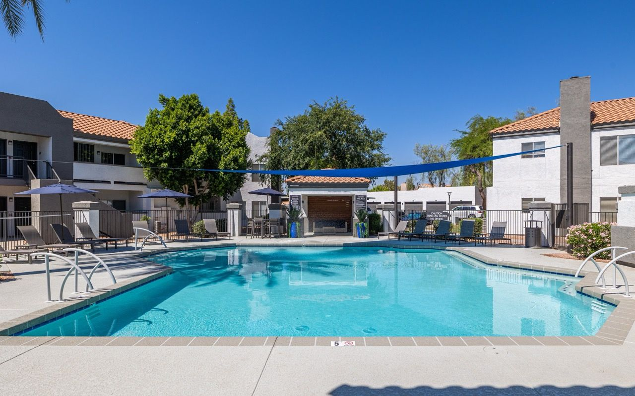 Outdoor apartment pool with lounge chairs, umbrellas, and a surrounding deck.