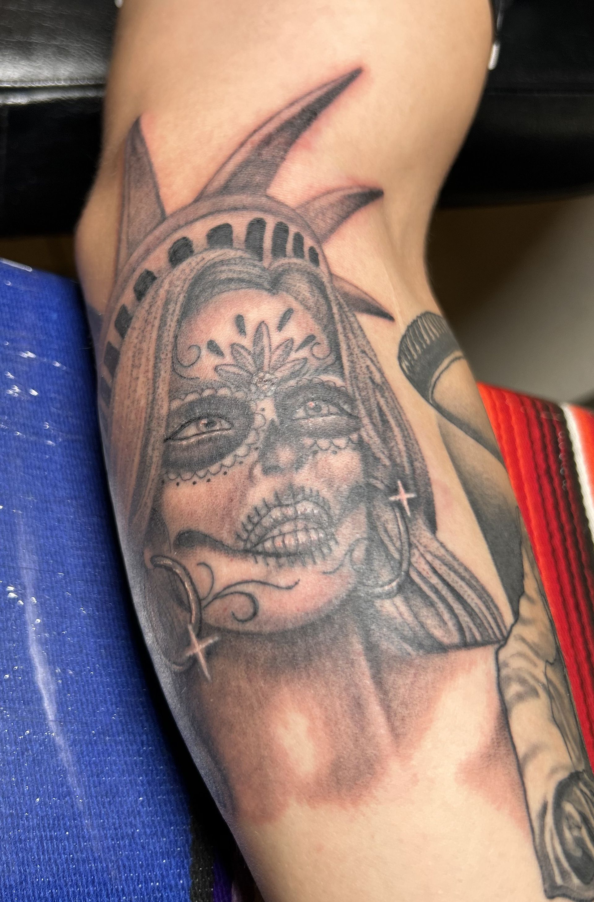 Tattoo of the Statue of Liberty stylized as a sugar skull, in black and gray ink.
