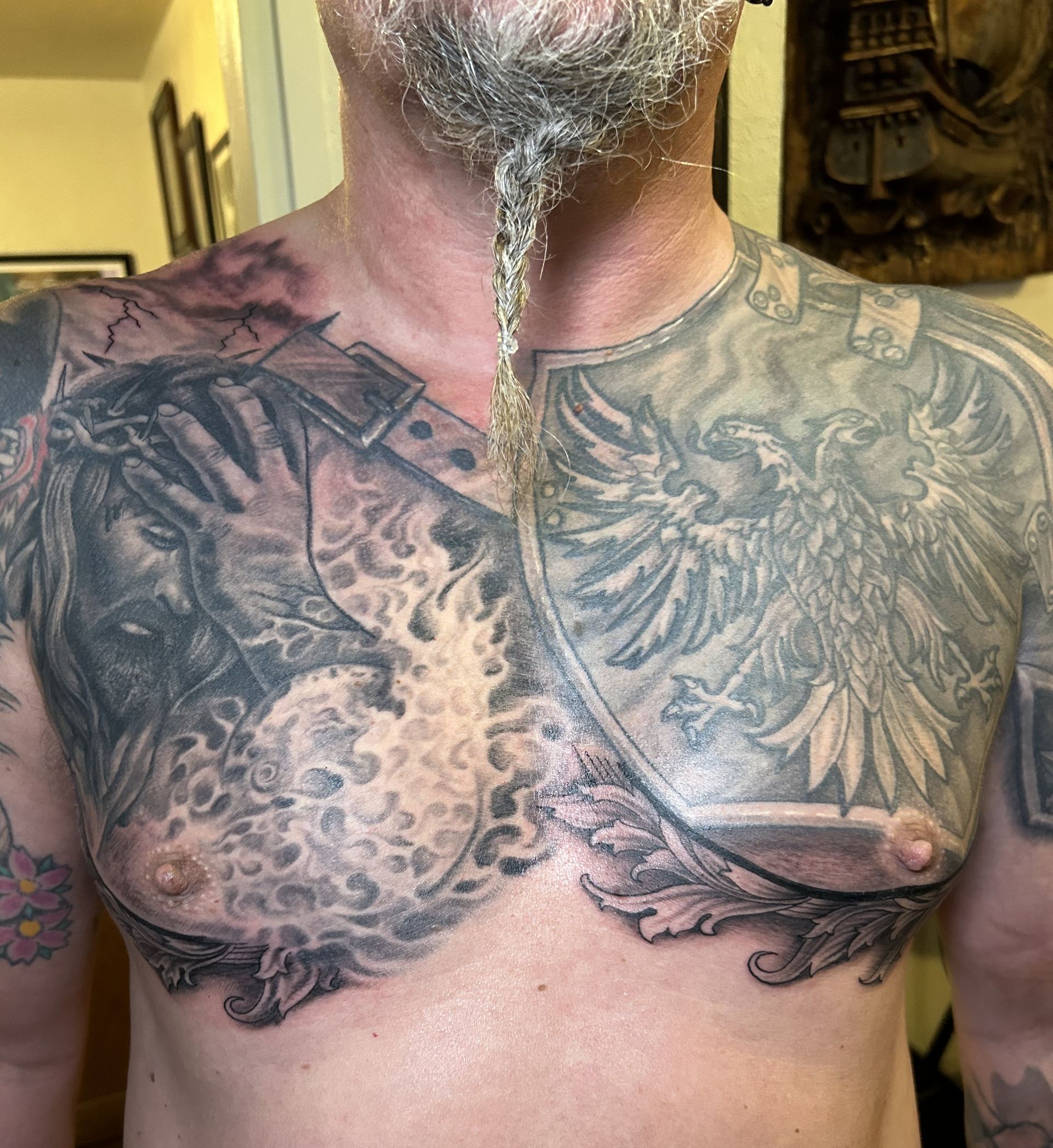 Man with elaborate chest tattoos: Jesus, eagle shield, and ornate designs.