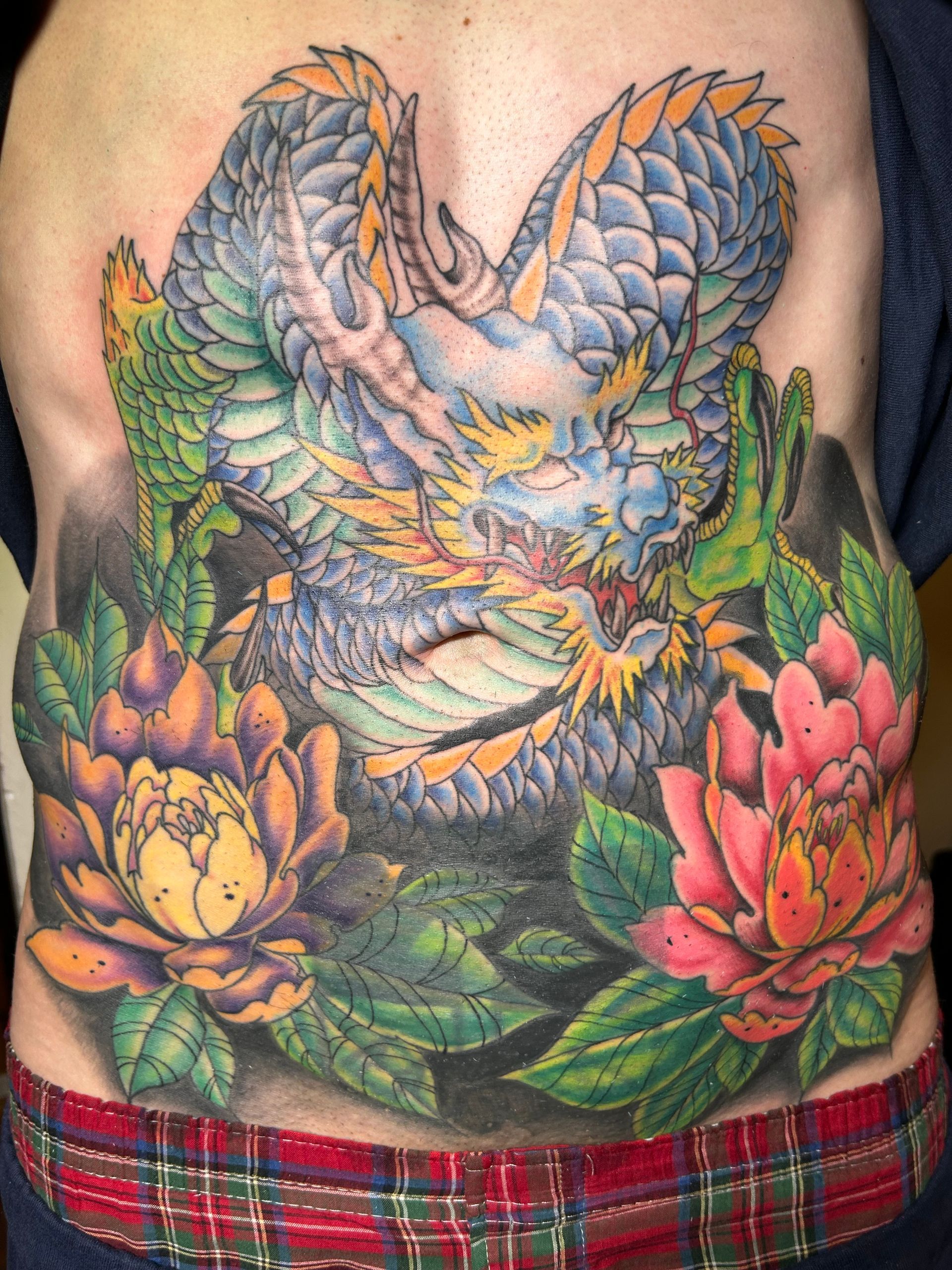 Dragon tattoo on torso with blue, green, and yellow scales, and flowers.