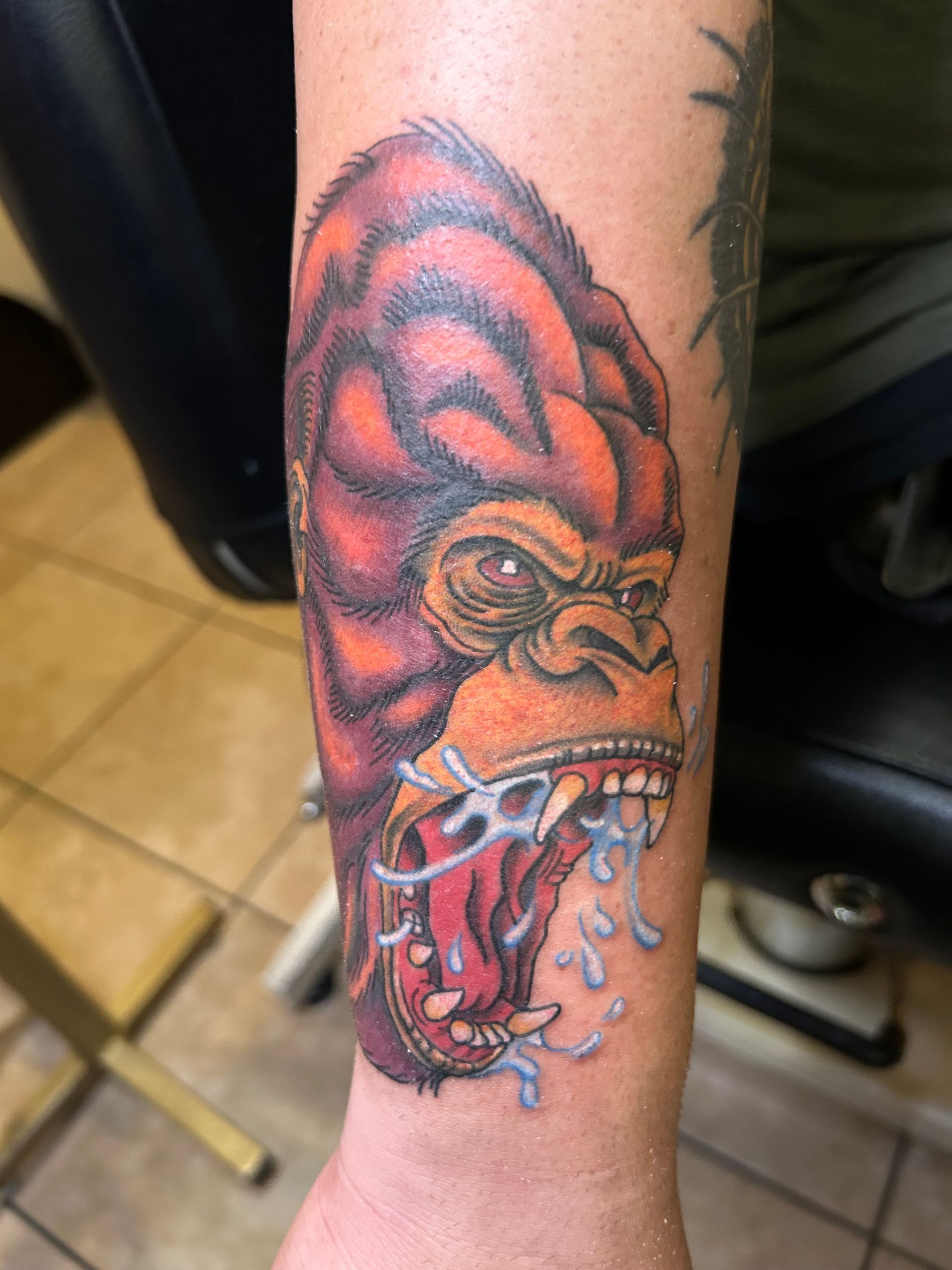 Tattoo of an angry, red and orange gorilla head with drool, on a person's forearm.