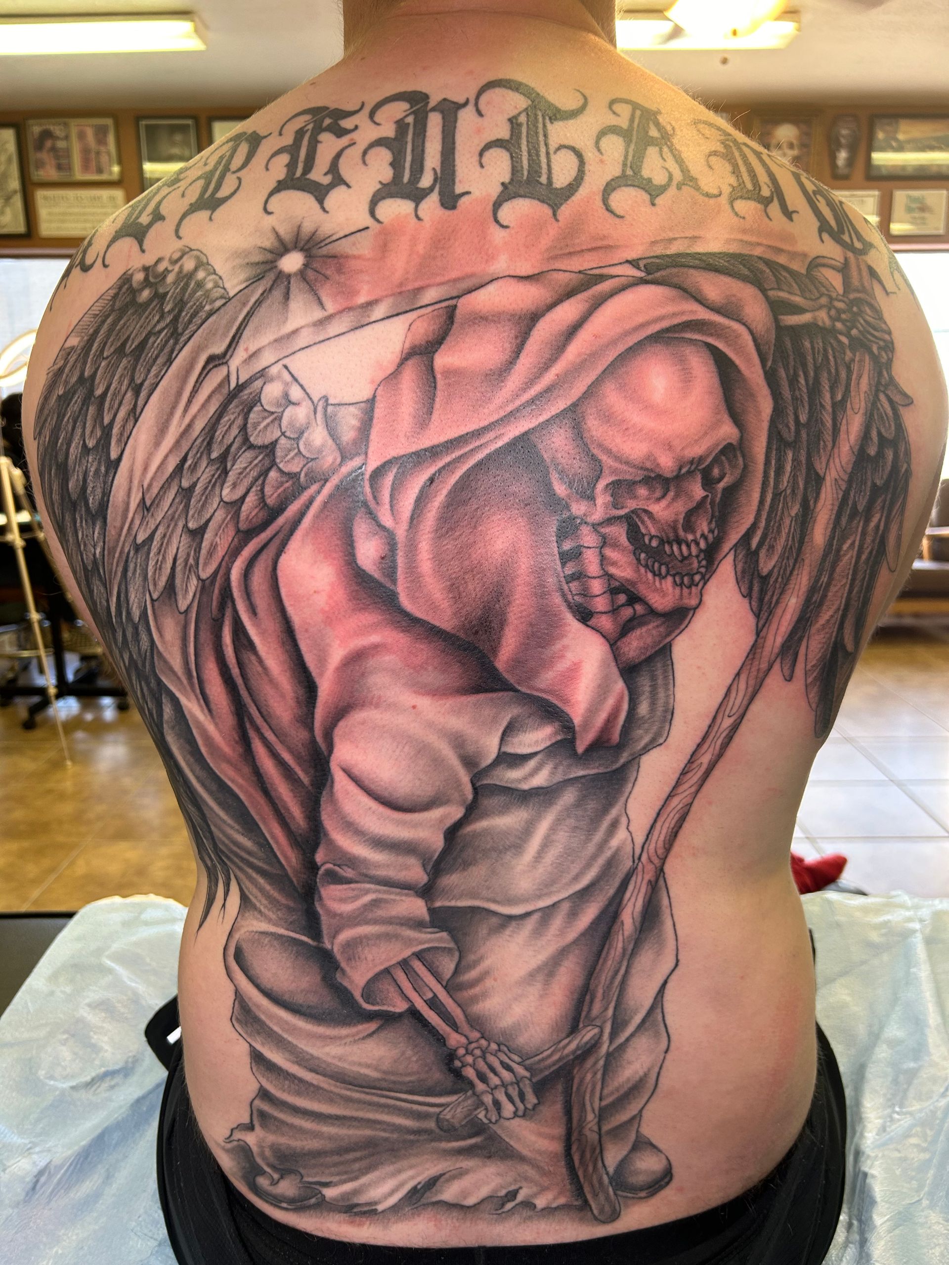Back tattoo: Grim Reaper in a hooded cloak with a scythe and angel wings, 
