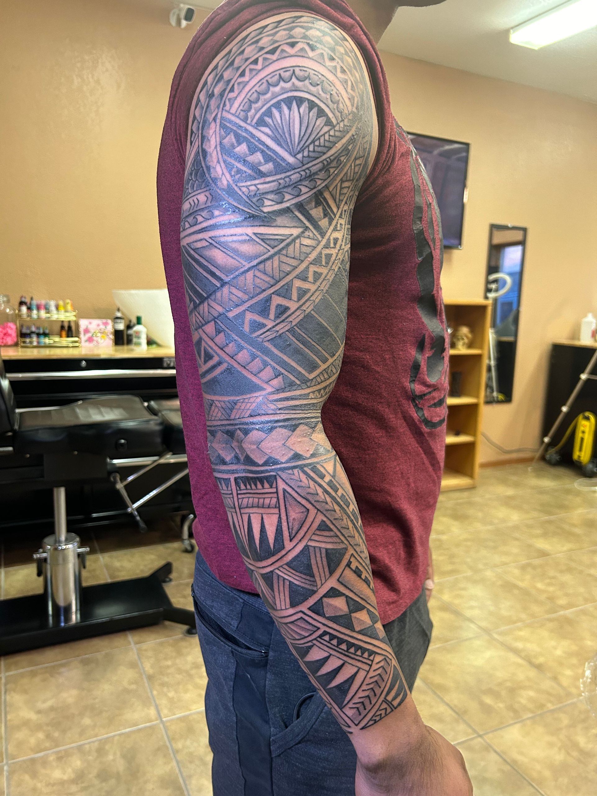 Man's arm with intricate black tribal tattoos, inside a tattoo parlor.