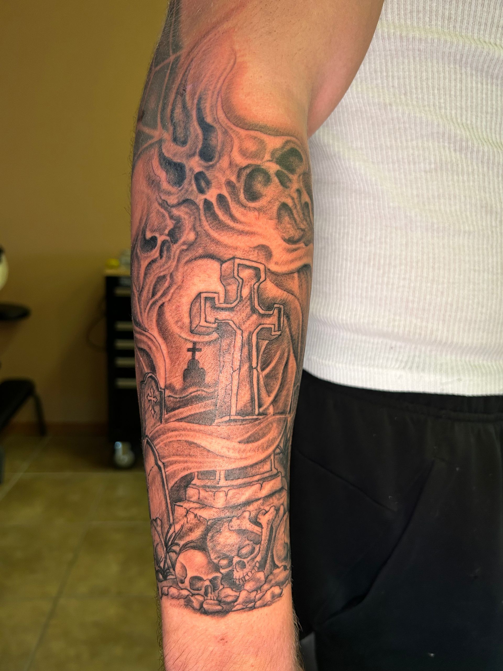 Arm tattoo: a cemetery scene with a cross, skulls, and smoke.