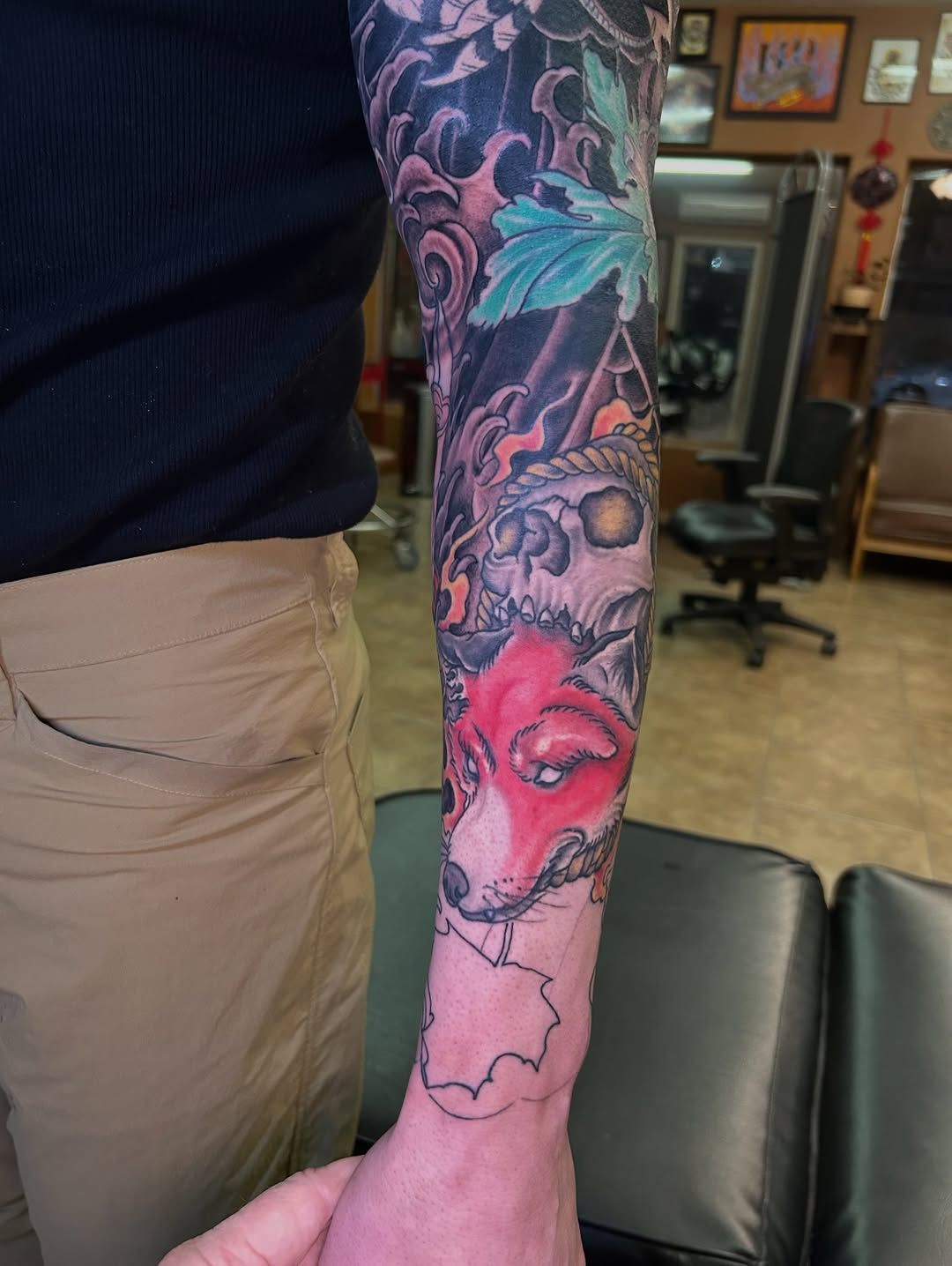Person with a sleeve tattoo featuring a red fox head, skull, and other dark imagery.