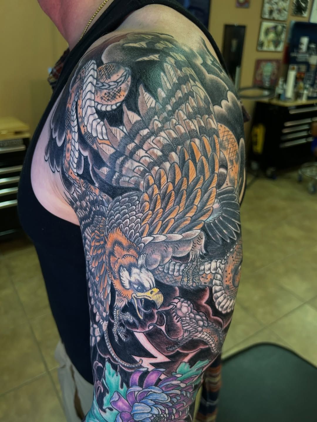 Arm tattoo depicting an eagle attacking a snake; vibrant colors, detailed, Japanese-inspired style.