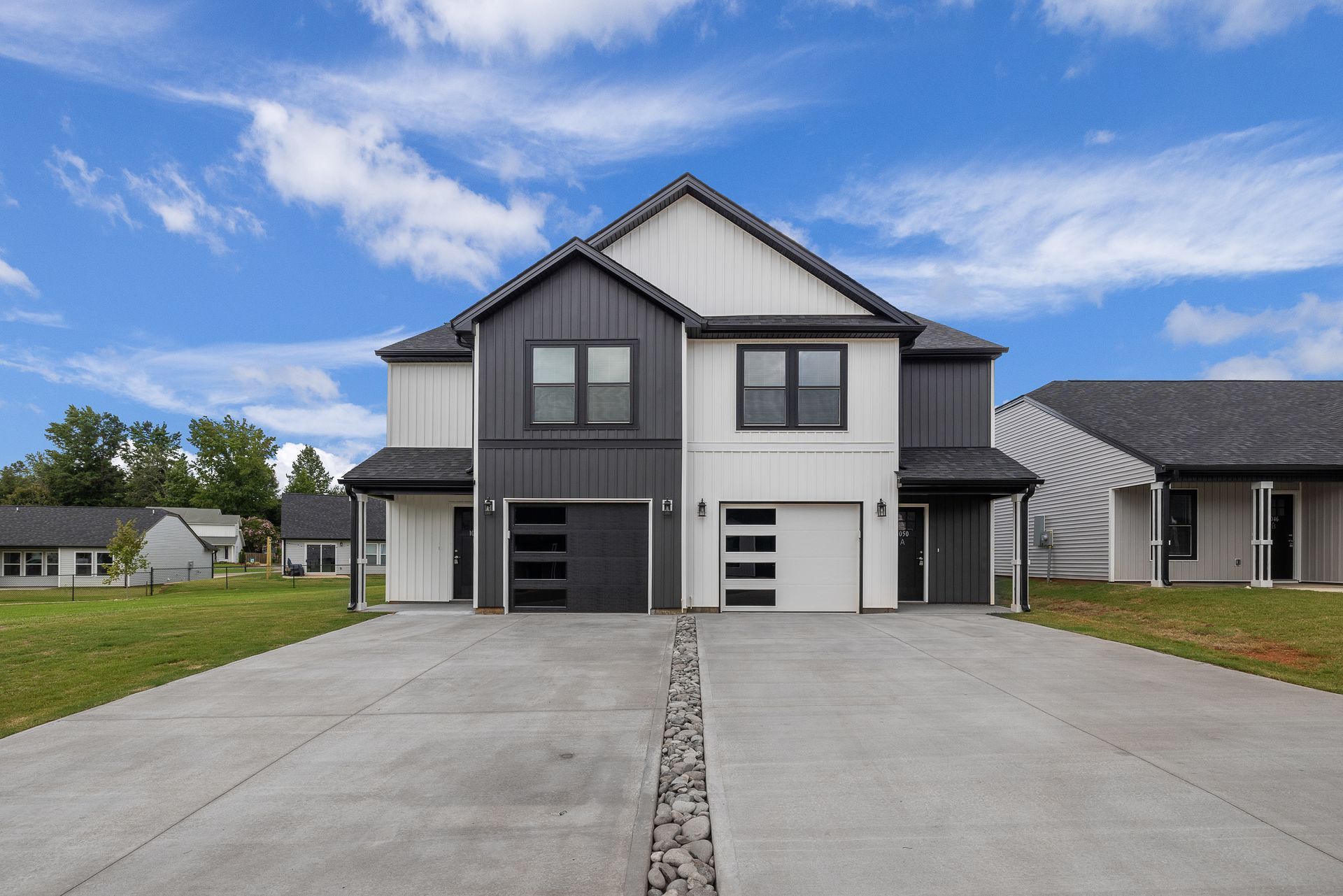 Modern duplex with gray and white siding, garages, and a concrete driveway under a blue sky.
