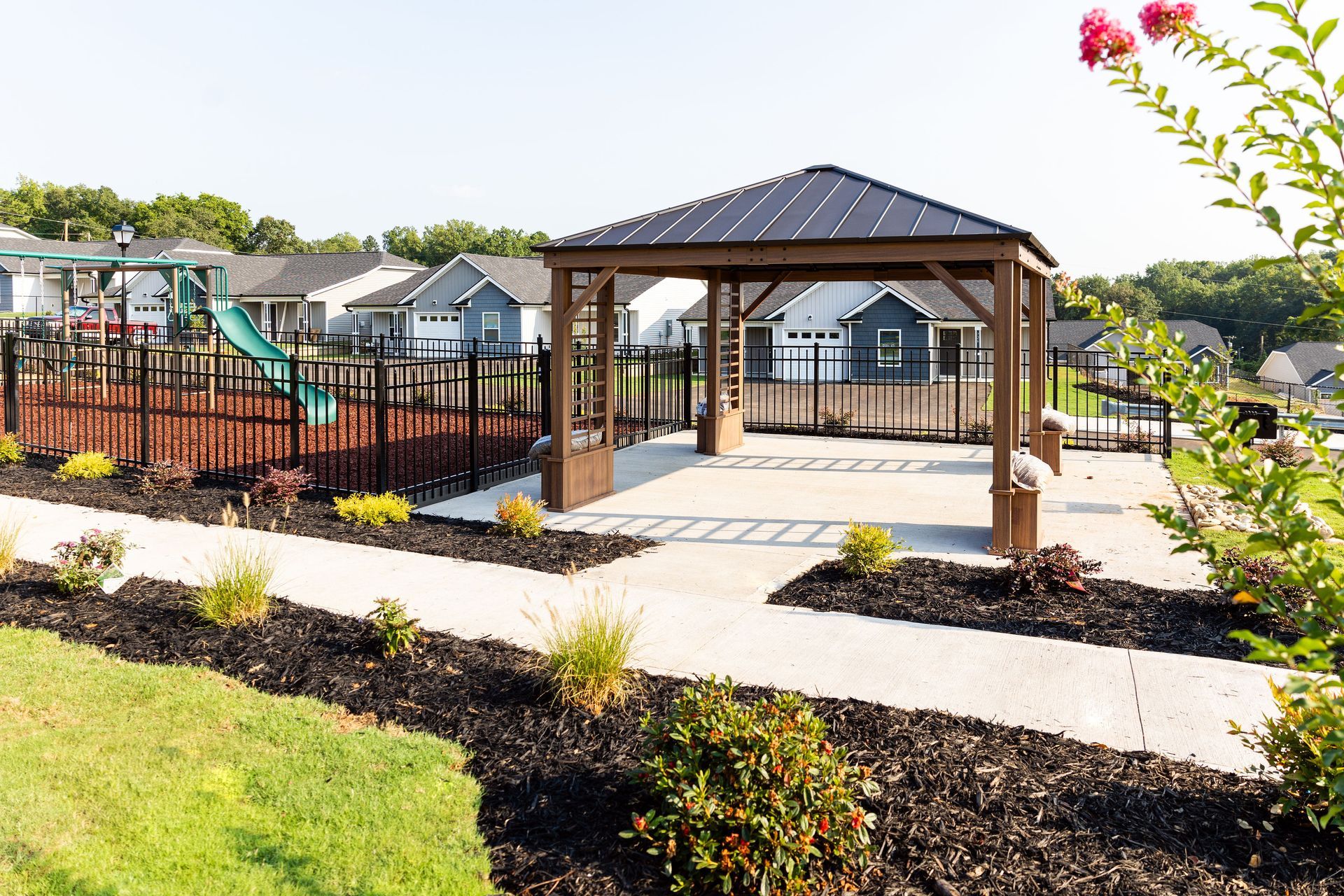 Gazebo in a park setting with houses in the background. Features a playground and landscaping.