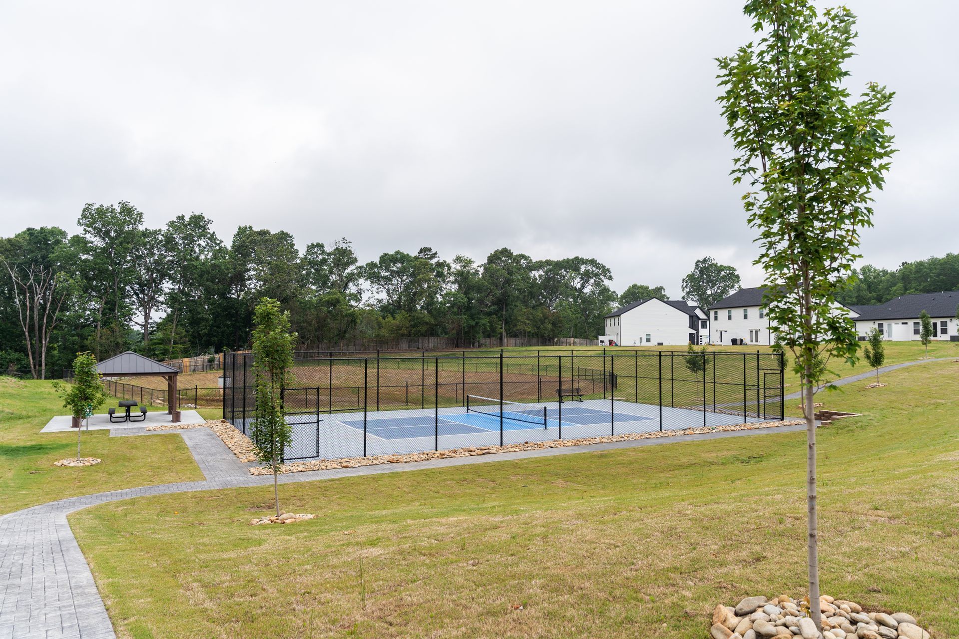 Modern duplex with dark gray and white siding, concrete driveway, and a cloudy sky.