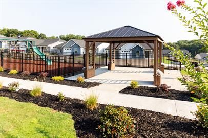 Gazebo in a park setting with houses in the background. Features a playground and landscaping.