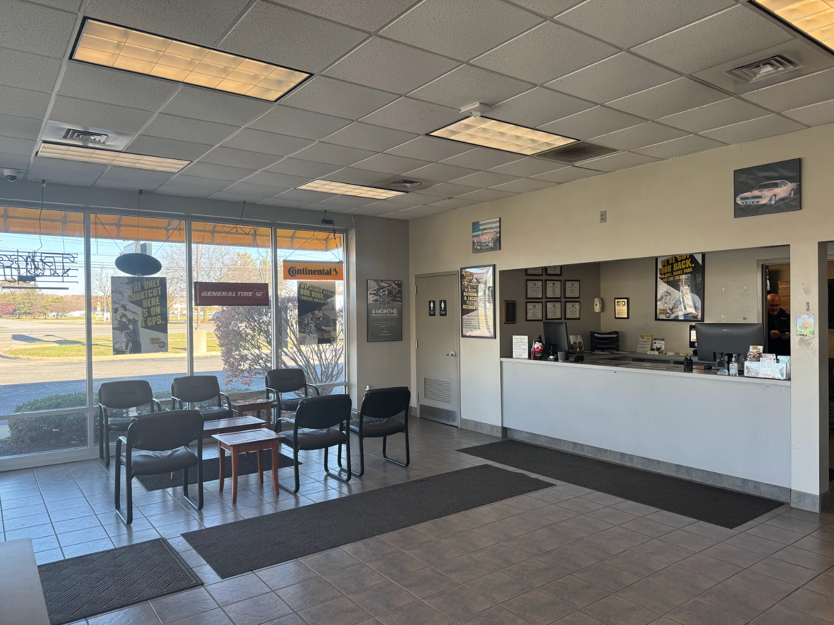 Waiting area inside a tire shop, with chairs, a counter, and large windows.