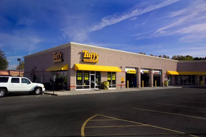 Exterior view of a Tuffy auto repair shop with yellow signage and awnings, white SUV parked outside.