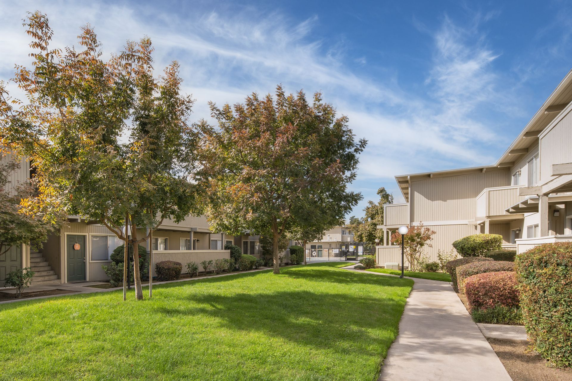 Grassy courtyard between beige apartment buildings under a blue sky with trees.