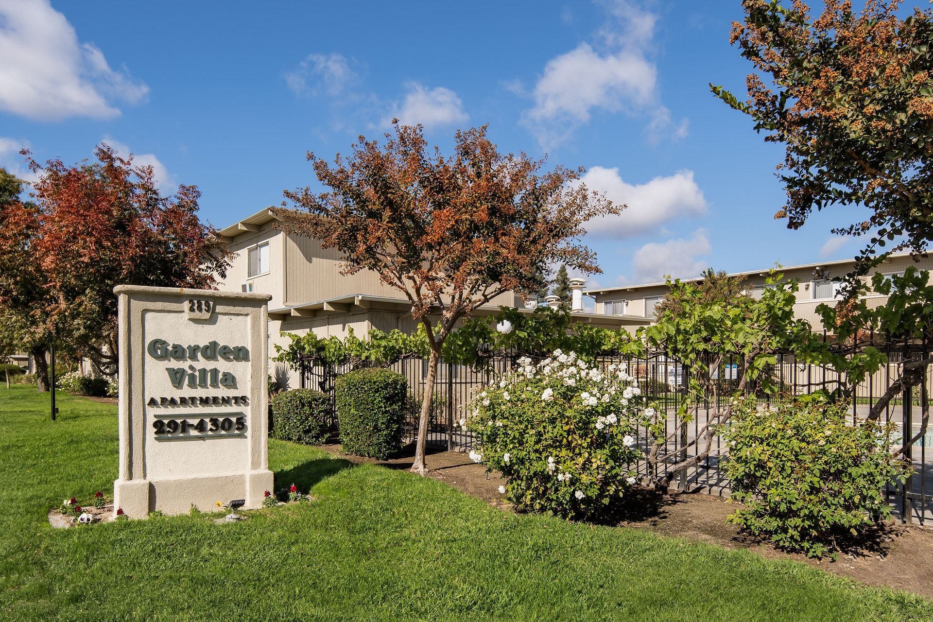 Garden Villas apartment sign with a building, trees, and fence.