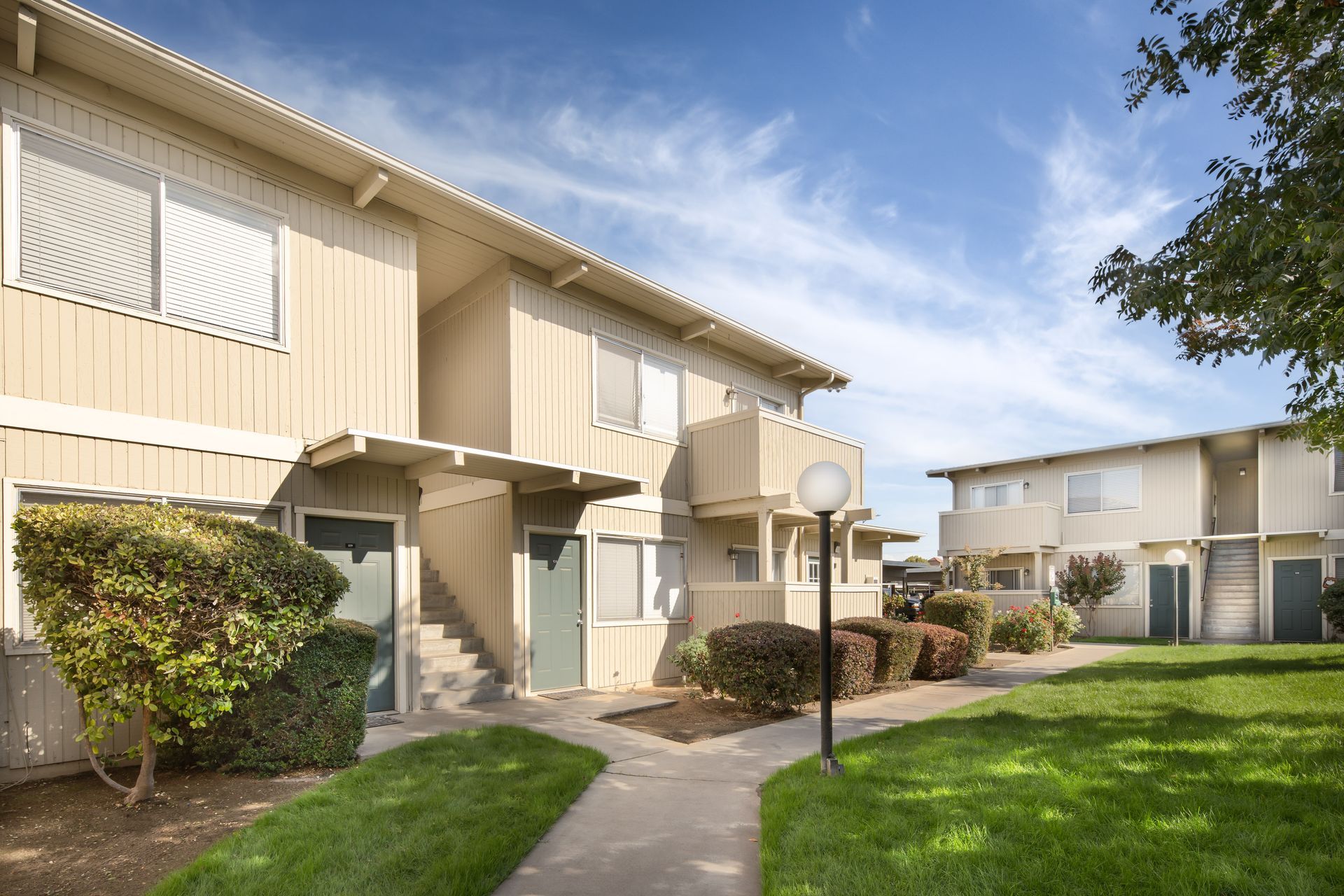 Apartment complex with beige buildings, green grass, and blue sky.