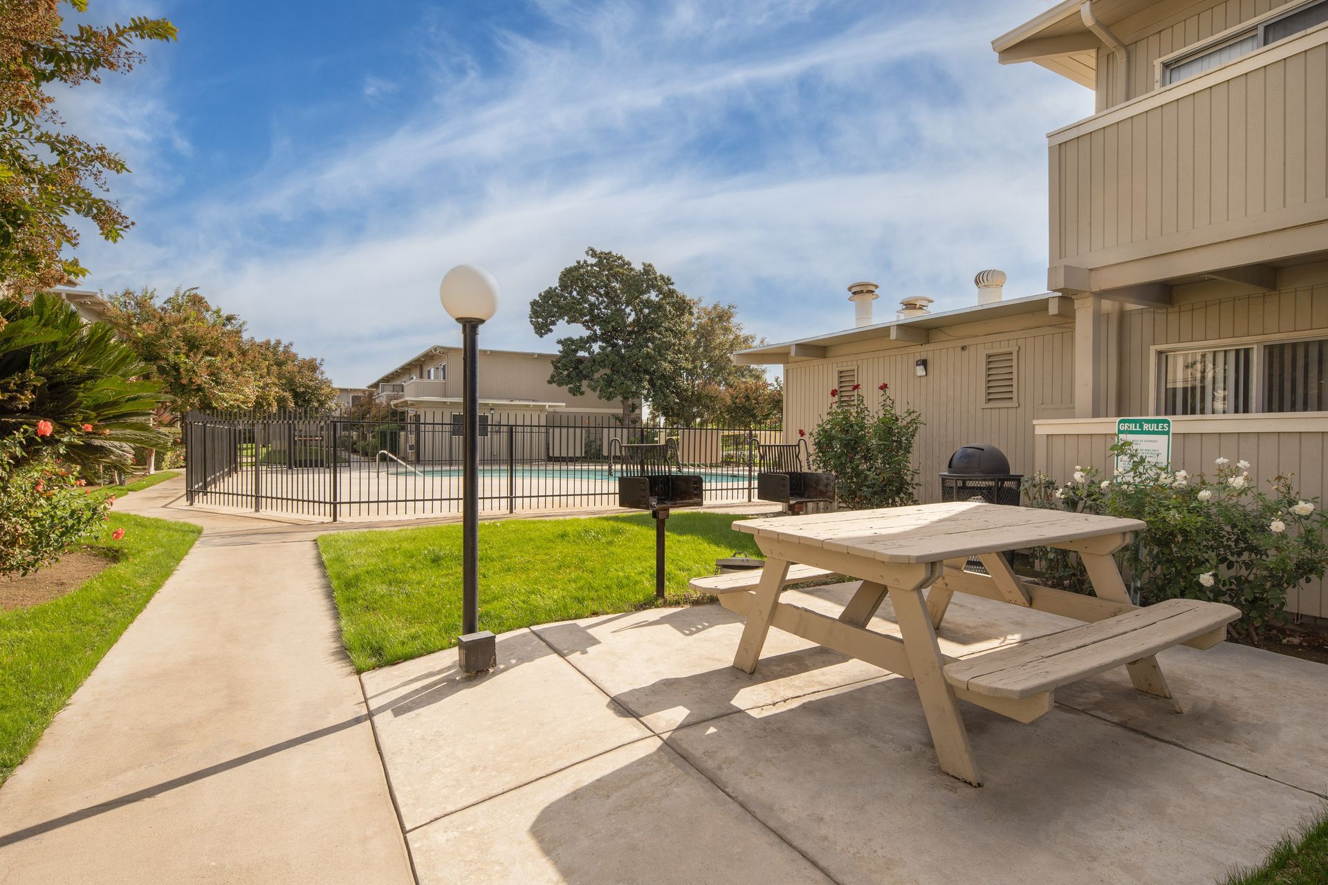 Picnic table and grill near pool, building in background on sunny day.