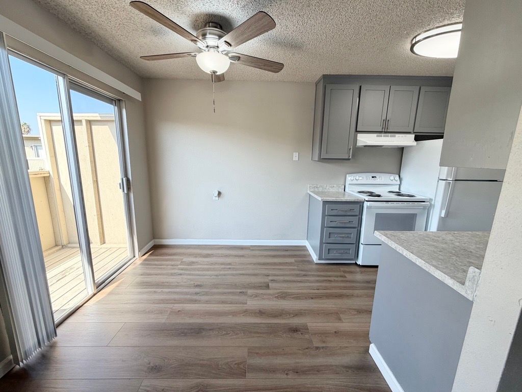 Interior of a kitchen/dining area with light brown flooring, gray cabinets, white appliances, and a sliding glass door.