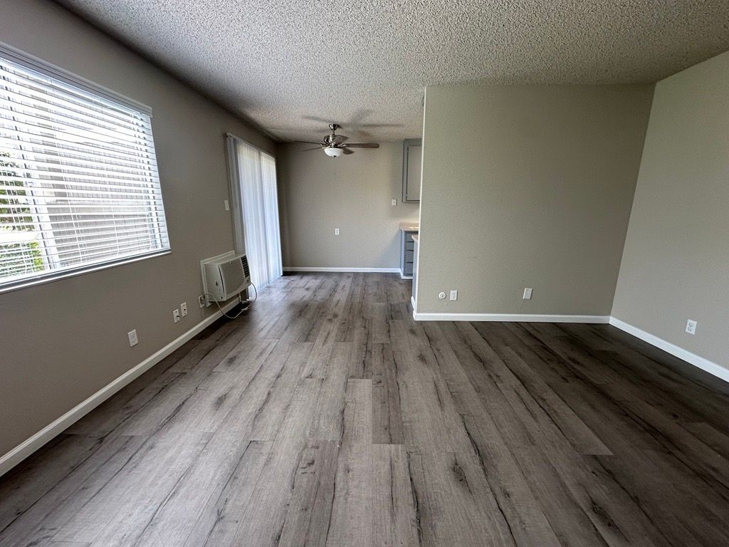 Empty living room with gray wood-look flooring and walls, window with blinds, and ceiling fan.