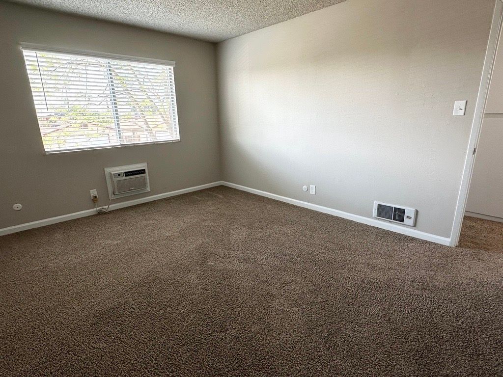Empty room with brown carpet, window with blinds, and neutral-colored walls.