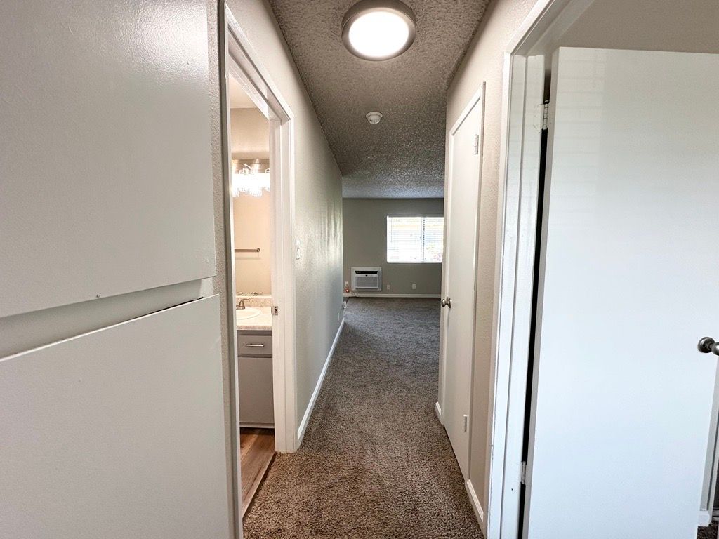 Hallway with doors on each side, leading to a bathroom and a room with a window.