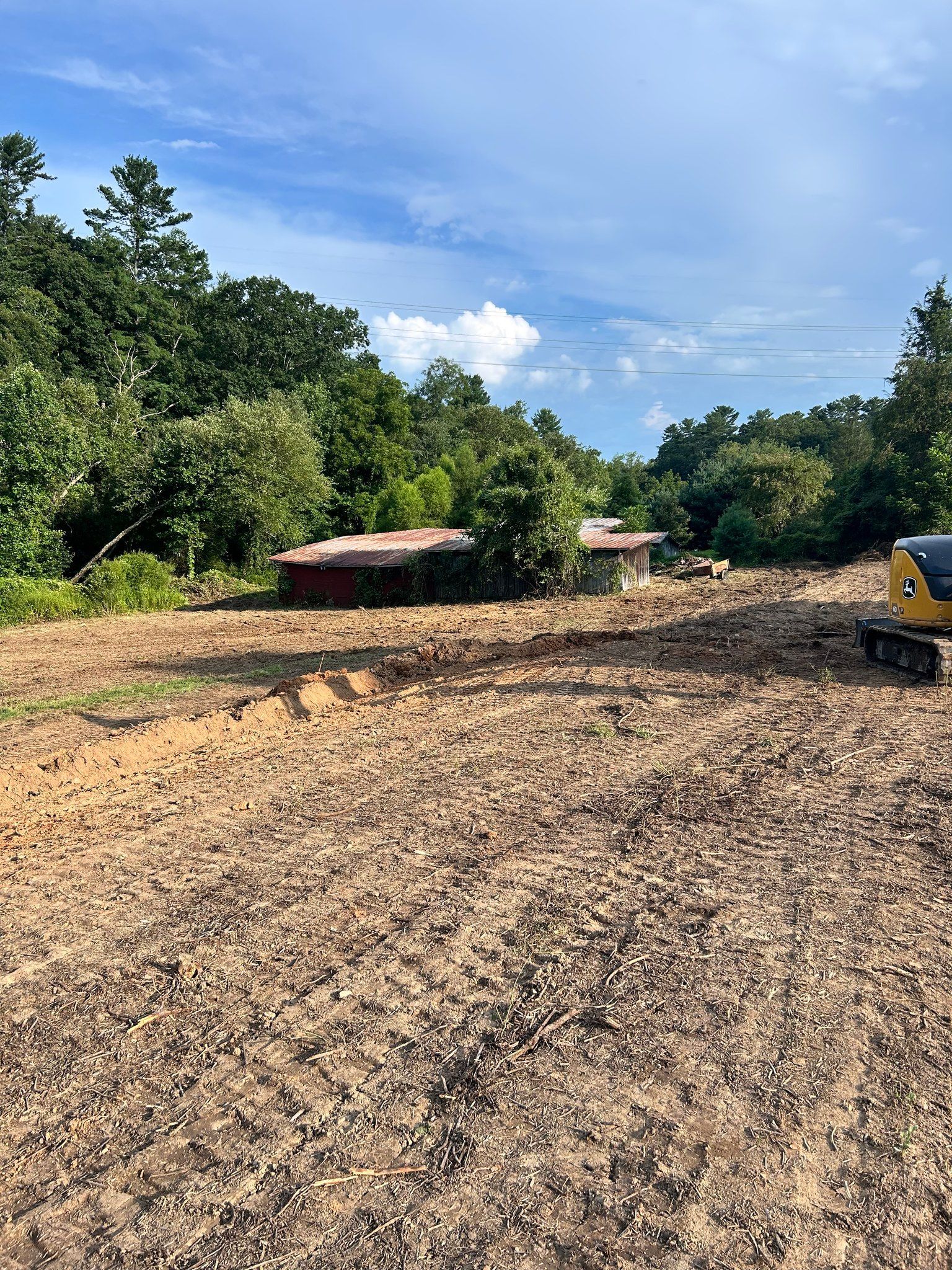 Cleared land with small buildings partially hidden by trees, blue sky.