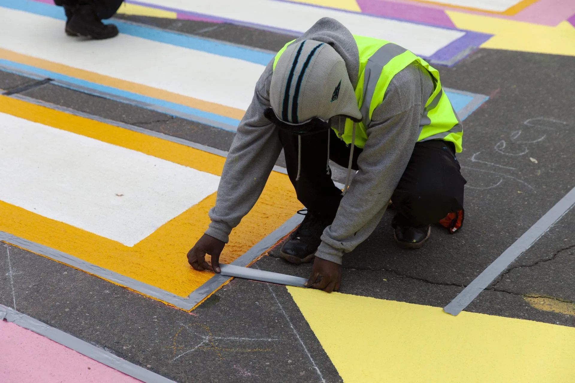 A man in a yellow vest is measuring a yellow line on the ground
