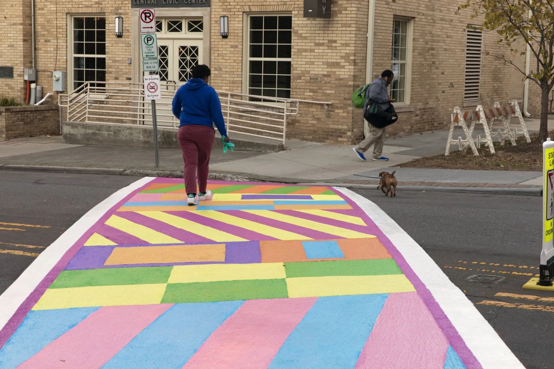 A woman is walking across a rainbow painted crosswalk