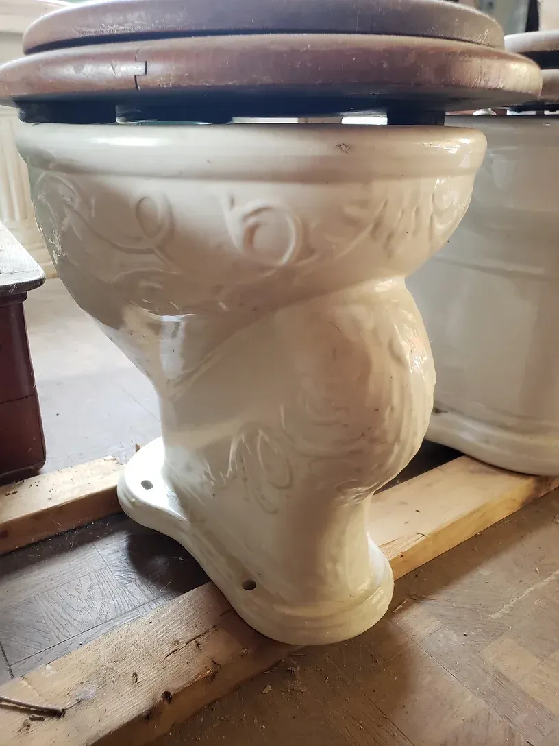 A white toilet with a wooden seat is sitting on a wooden pallet.