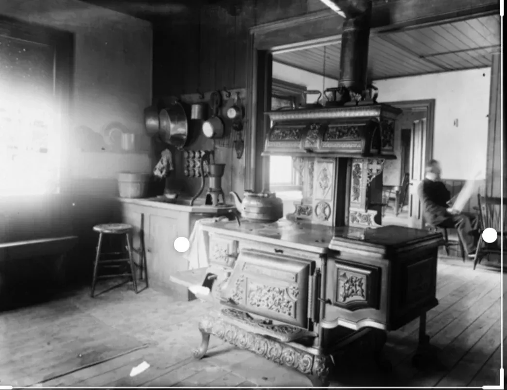 A black and white photo of a kitchen with a wood stove