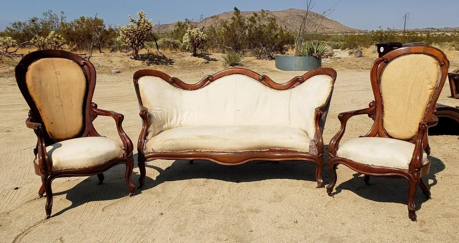 A couch and two chairs are sitting in the middle of a desert.