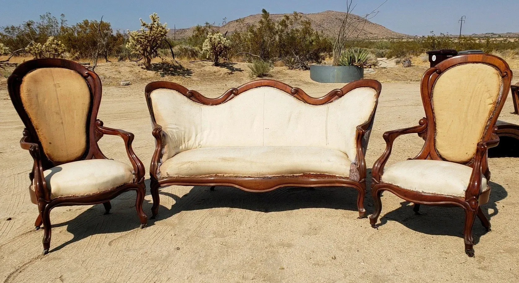 A couch and two chairs are sitting in the middle of a desert.
