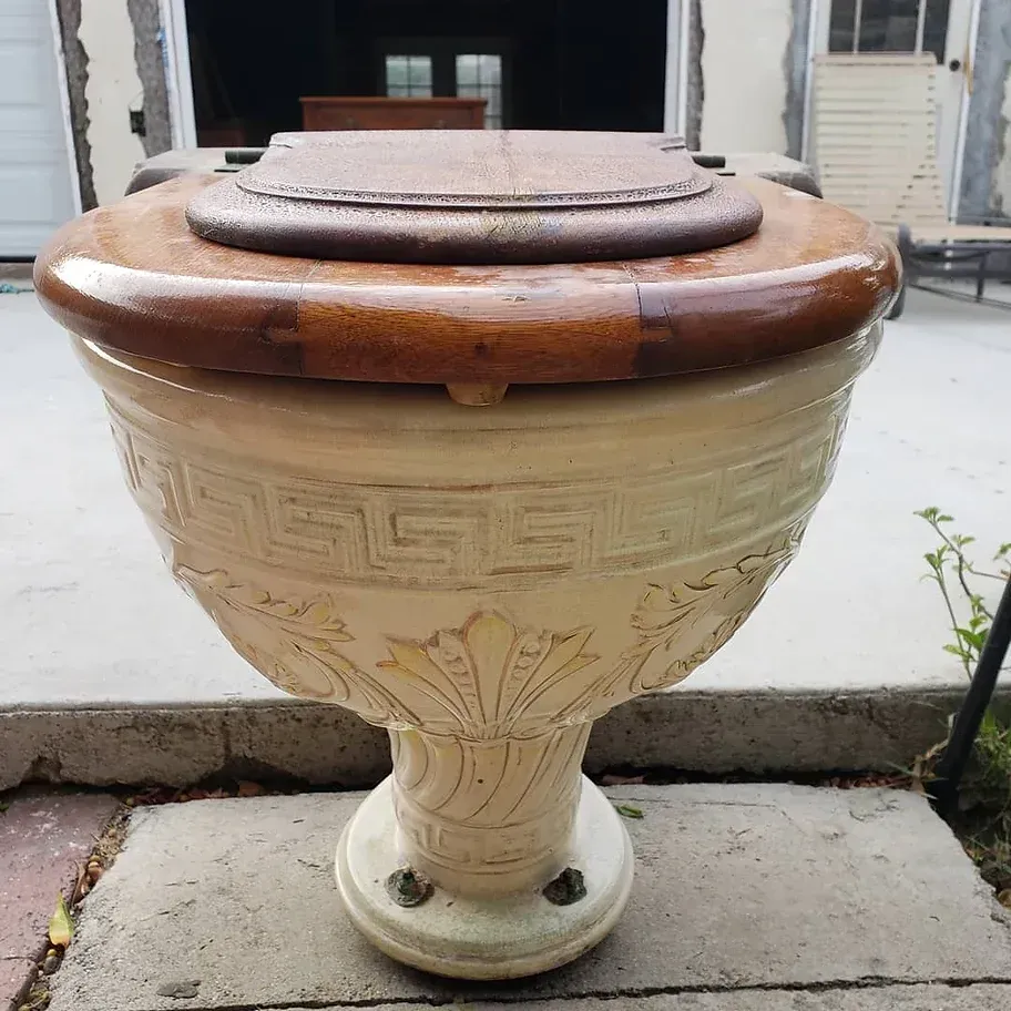 A white vase with a wooden lid has a greek key design on it