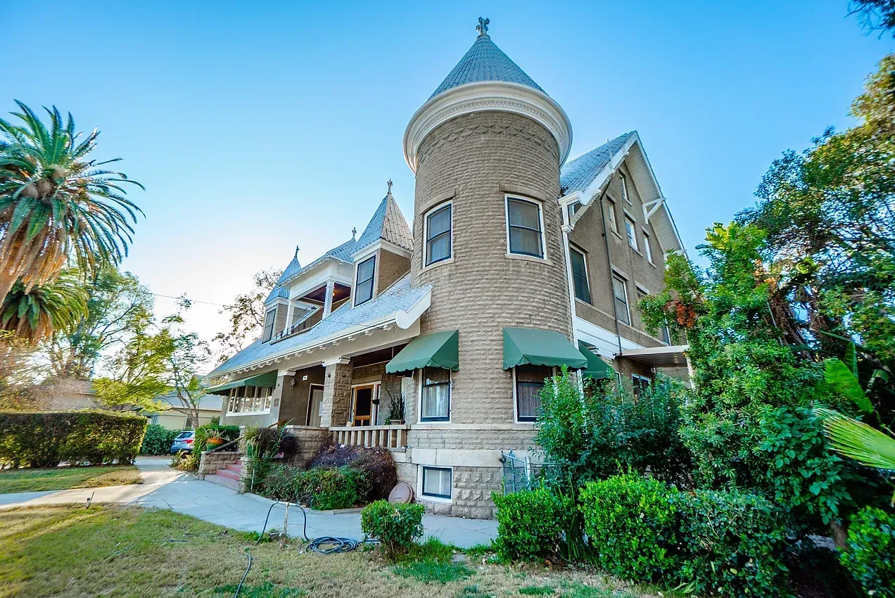 A large brick house with a tower on top of it surrounded by trees and bushes.