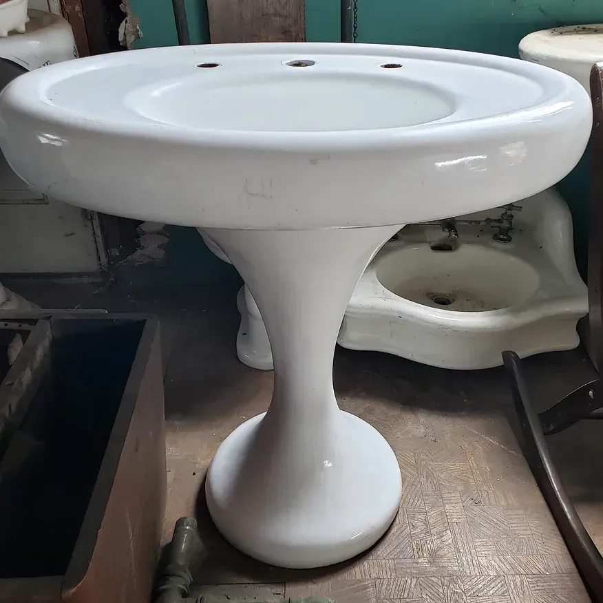 A white pedestal sink is sitting on top of a wooden table.