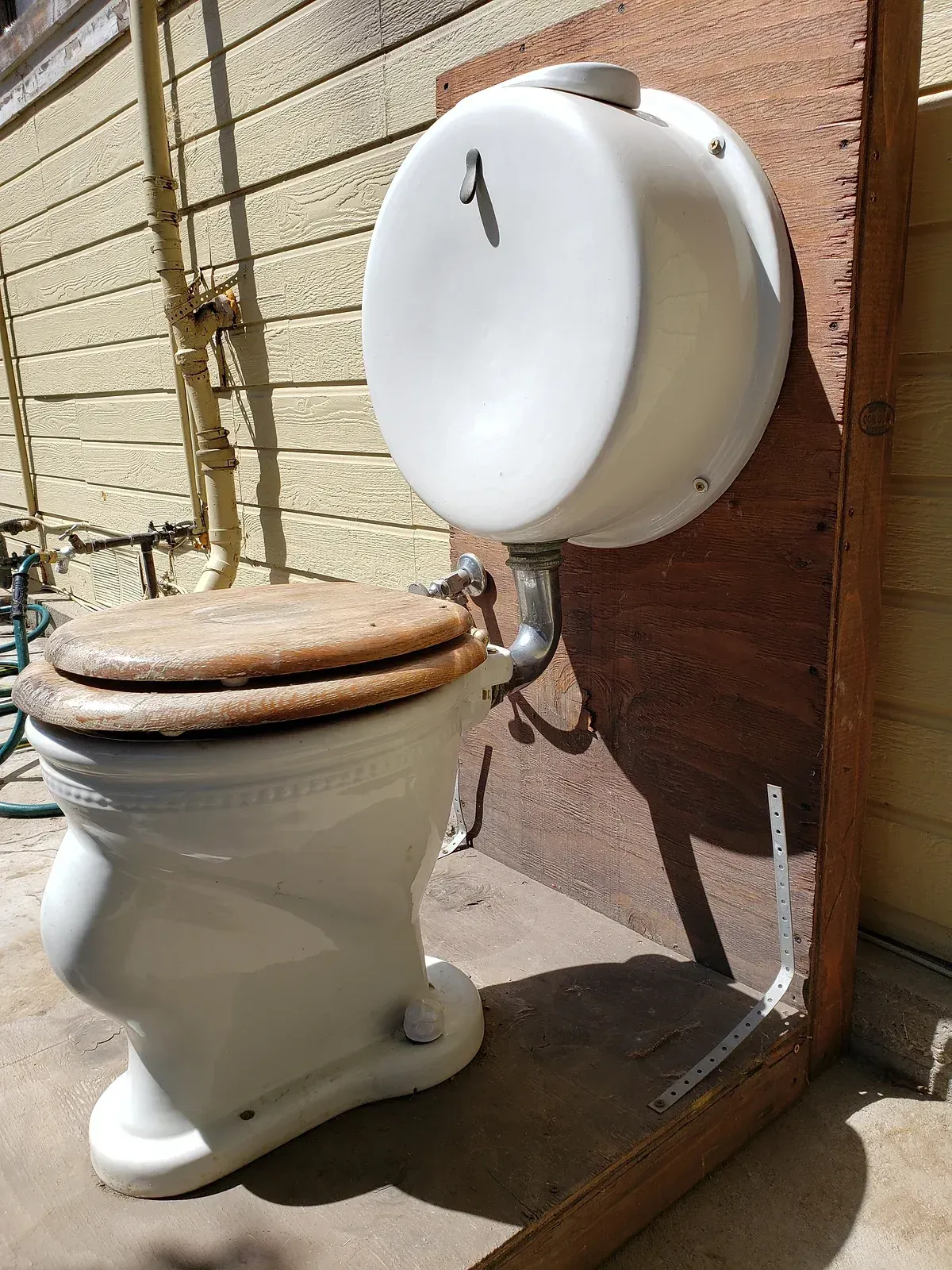 A white toilet with a wooden seat is sitting next to a wooden wall.