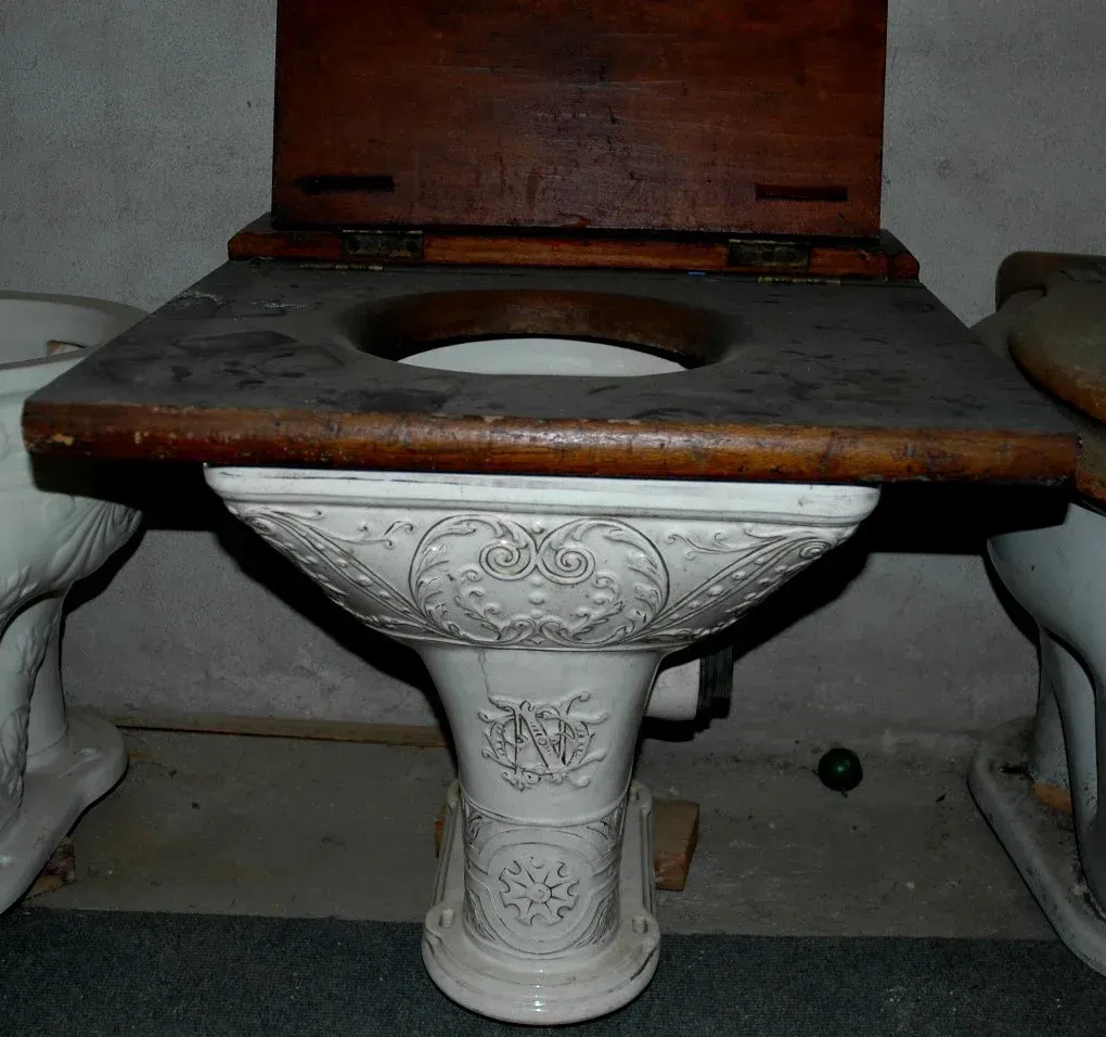 A toilet with a wooden seat sits next to two other toilets