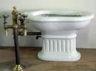 A white toilet with brass faucets is sitting on a wooden floor.