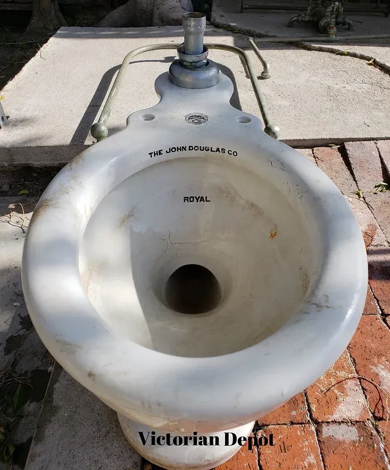 A white toilet is sitting on top of a brick floor.