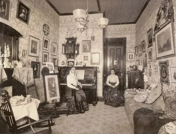Two women are sitting in a living room with a piano.