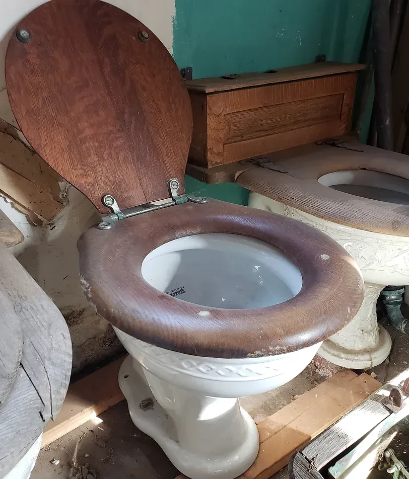 An old toilet with a wooden seat is sitting on a wooden floor.
