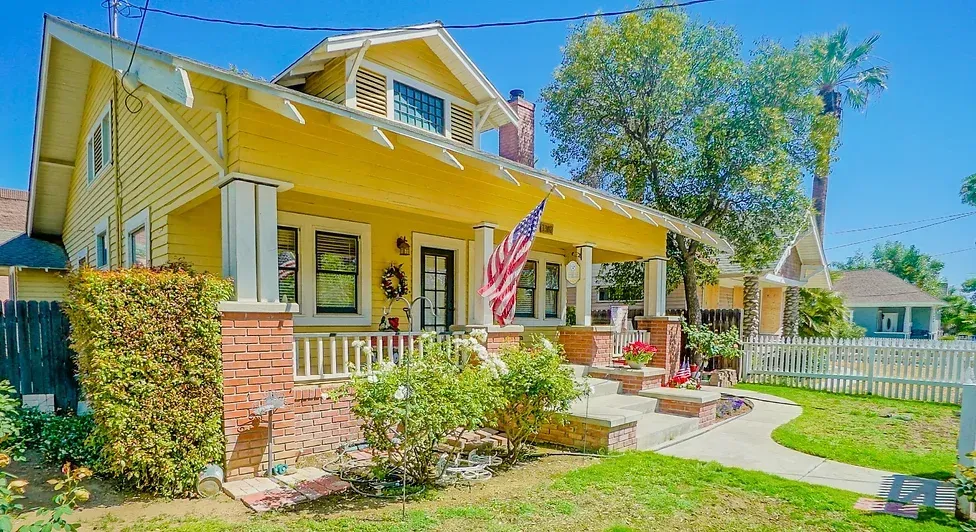 A yellow house with an american flag on the porch.