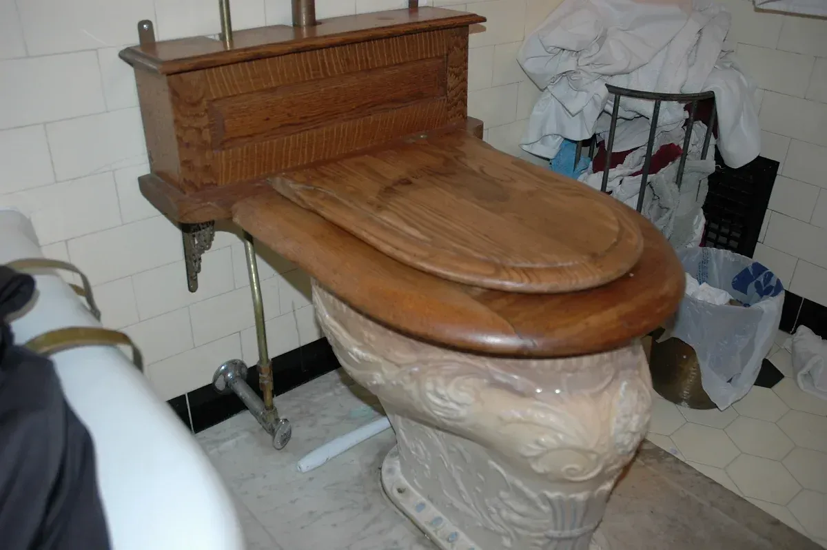 A wooden toilet sits in a bathroom next to a trash can