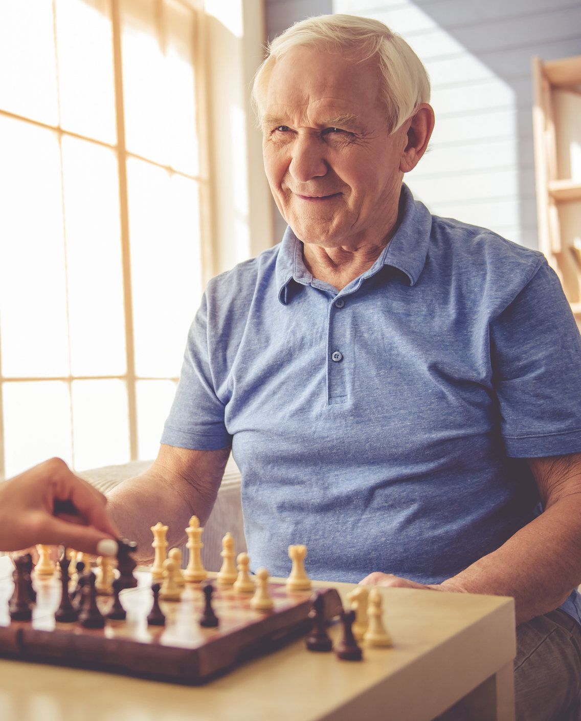 An elderly man is playing a game of chess with a caregiver.