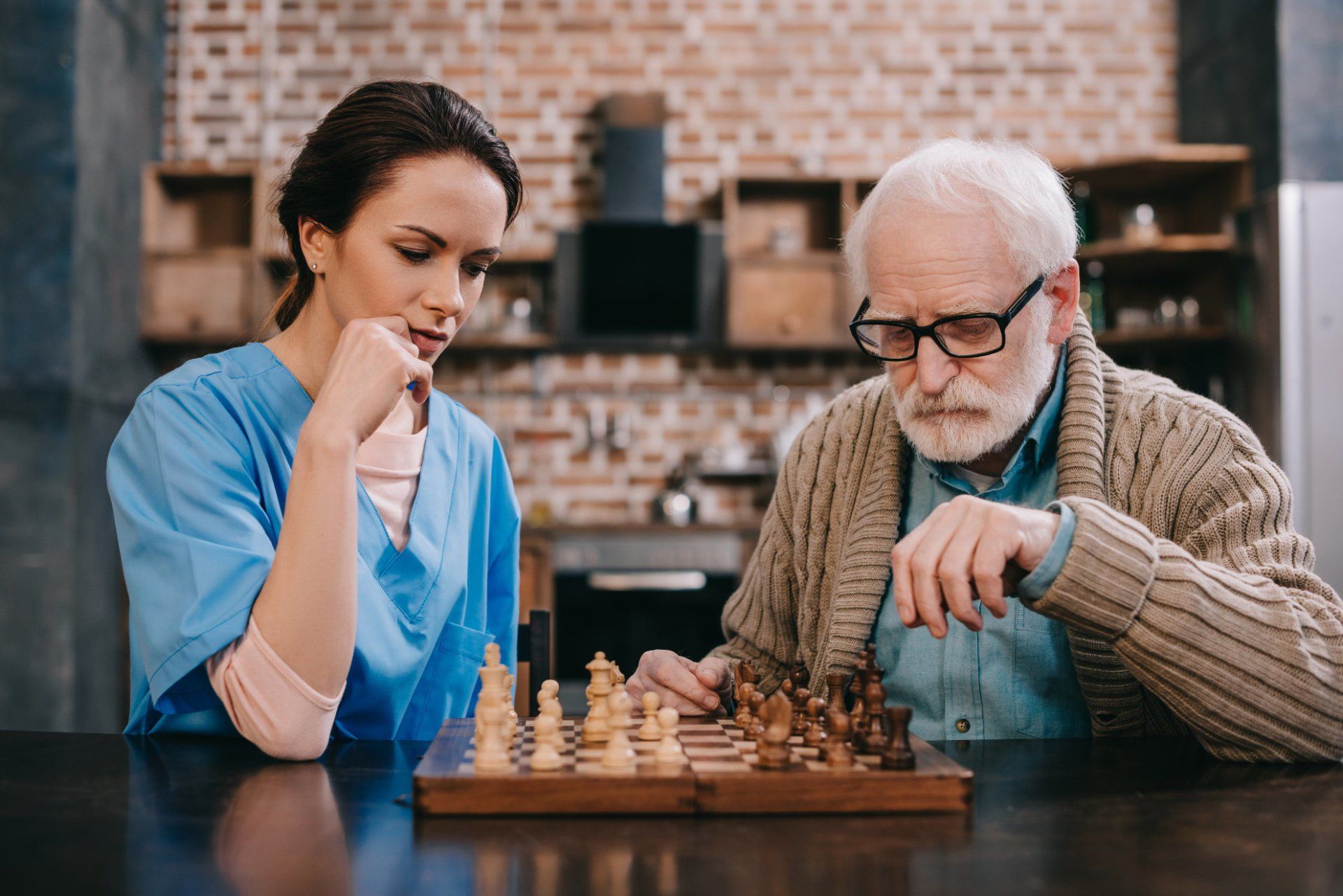 A nurse is helping an elderly man play chess.
