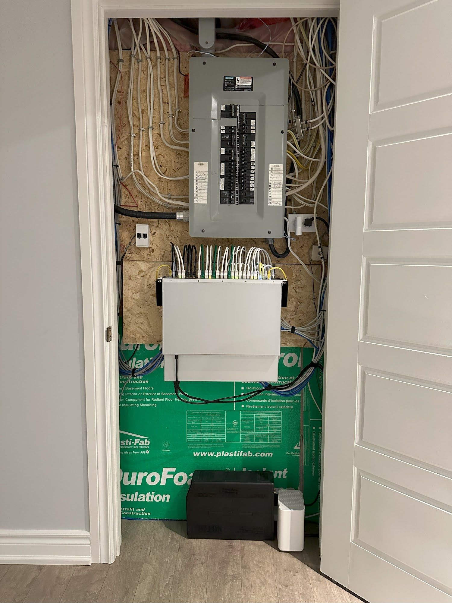 Electrical panel and network equipment in a closet, various wires, green insulation, white doors.