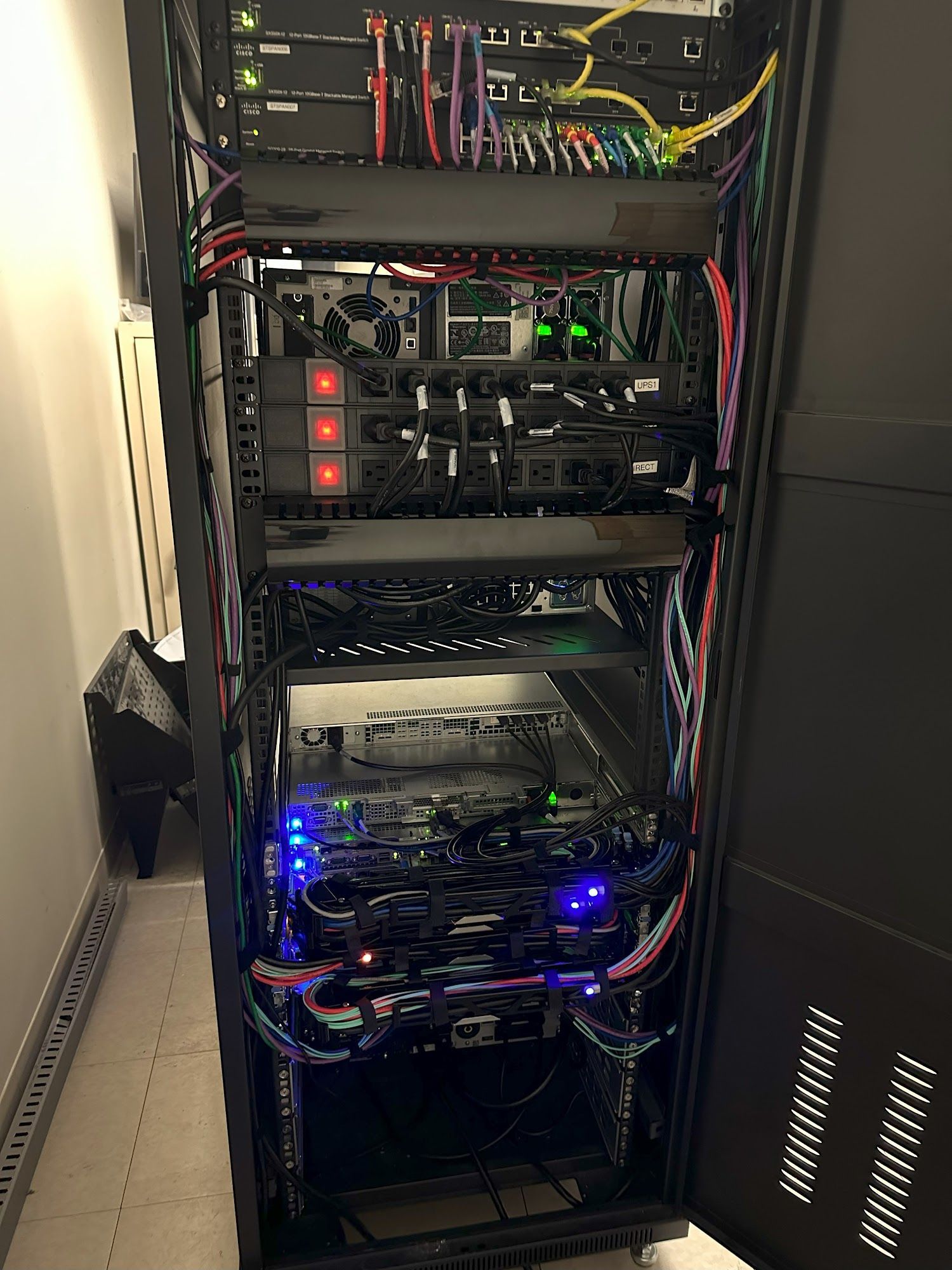 Server rack with various networking devices, cables, and lights. Dark room setting.